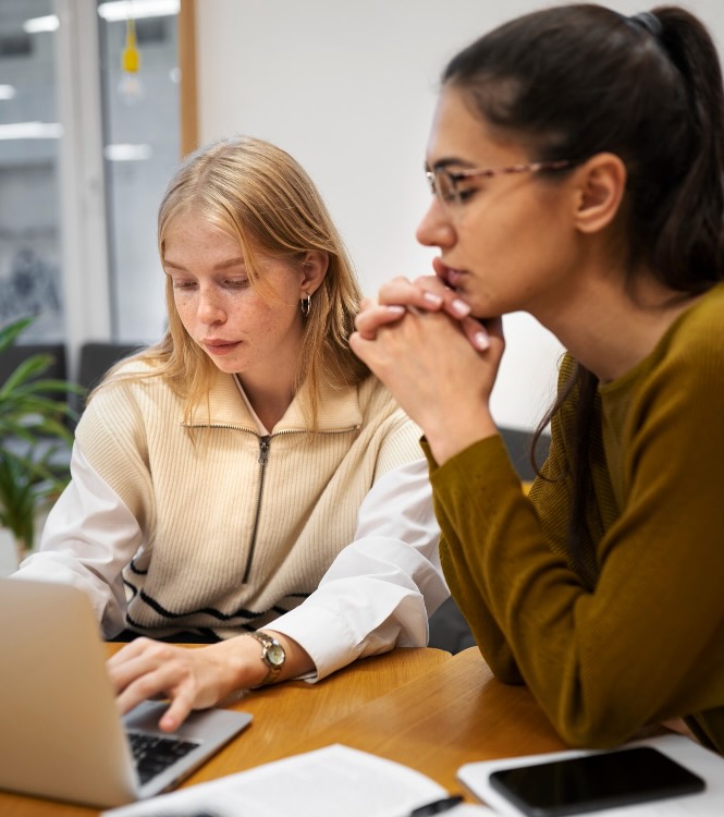 Diversity and Inclusion New Zealand - Unconscious Bias Programs background Unconscious Bias Programs: Two colleagues focused on a laptop screen, collaborating in a meeting room with open books
